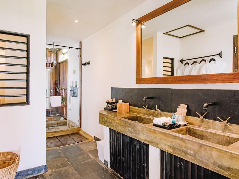 Helles Badezimmer mit zwei Waschbecken, großem Spiegel, dunklem Steinboden und Holzakzenten.