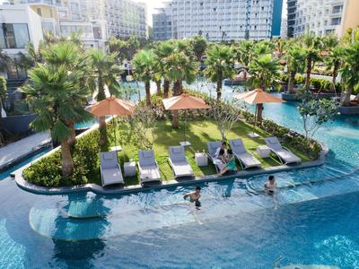 Piscina moderna de hotel con islas verdes, palmeras y huéspedes en el agua en un día soleado.