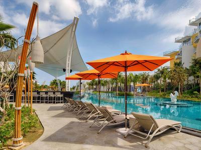 Moderner Poolbereich mit Liegestühlen und orangefarbenen Sonnenschirmen neben einem Hotel.