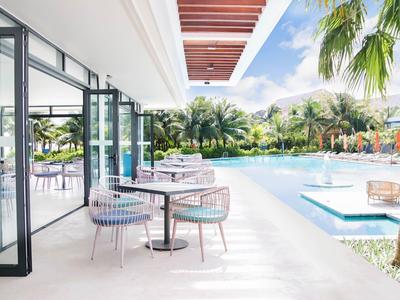 Moderner Außenbereich mit Sitzgelegenheiten, Glasfassade und Pool umgeben von Palmen bei Sonnenschein.