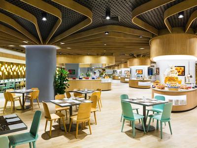 Comedor moderno y luminoso con techo de madera y varias áreas de asientos en un hotel.