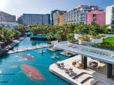 Moderner Hotelpool mit Sonnenschirmen, Liegestühlen und tropischer Landschaft bei Sonnenschein.