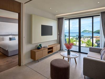 Sala moderna con sofá, mesa de centro, TV y grandes ventanales con vista al mar en la habitación del hotel.