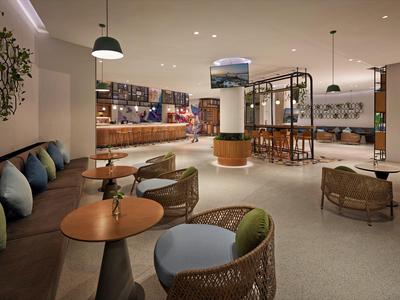 Área moderna de vestíbulo de hotel con mesas redondas, sillas cómodas y ambiente relajado.