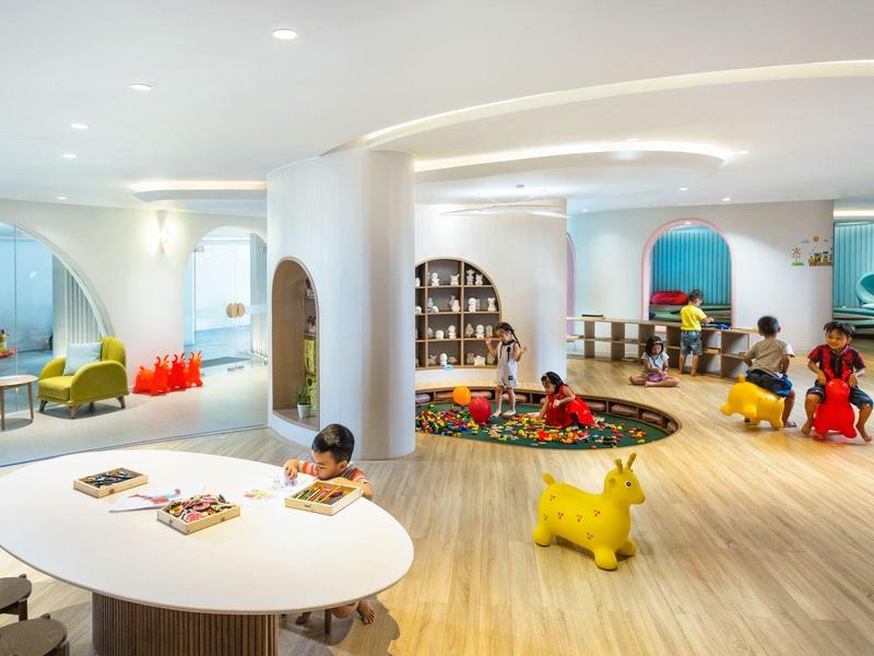 Área de juegos infantil luminosa y moderna en hotel, con muebles coloridos y suelo de madera.