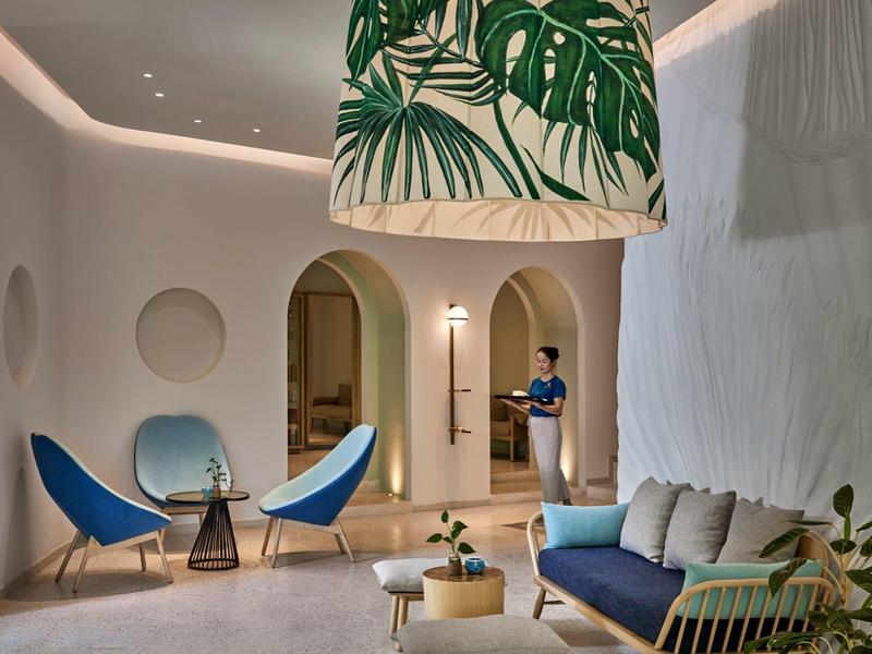 Sala moderna de hotel con sofá azul, sillas y lámpara decorativa de plantas.