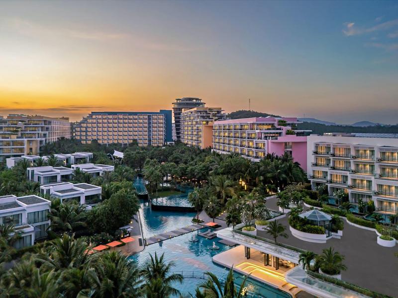Hotel de lujo con gran piscina y jardín tropical al atardecer junto al mar.
