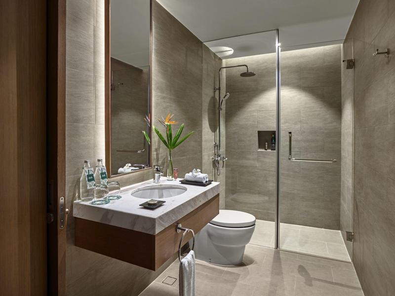 Baño moderno de hotel con ducha integrada, inodoro y lavabo sobre azulejos grises.