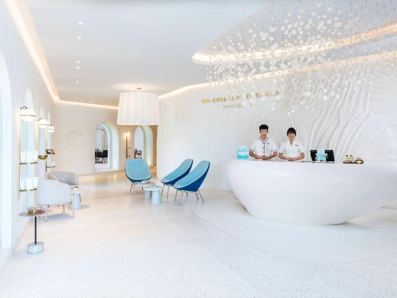 Moderna y luminosa recepción de hotel con mobiliario blanco, mostrador y dos empleados.