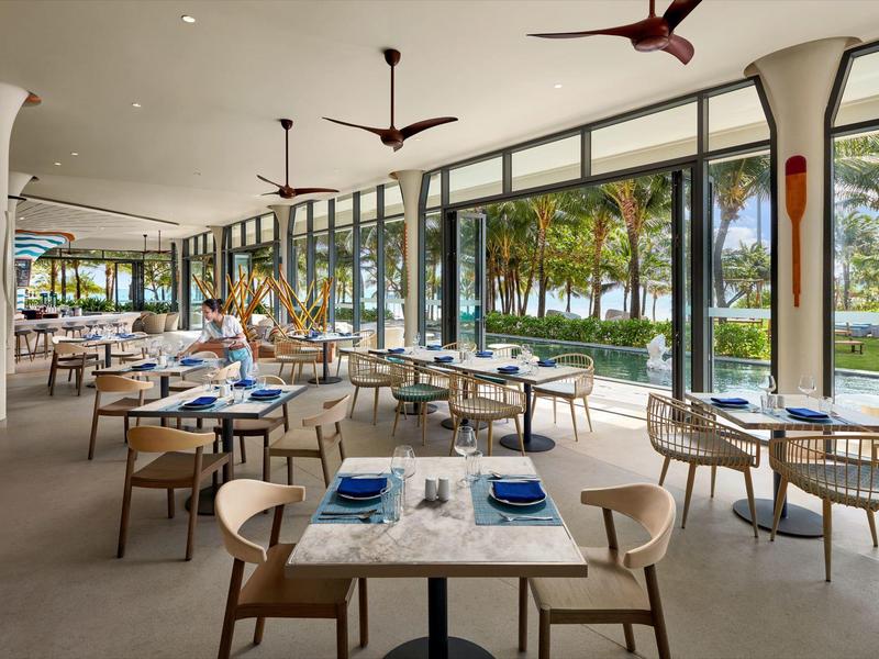 Restaurante moderno con terraza y vista a jardín tropical y acceso al agua.