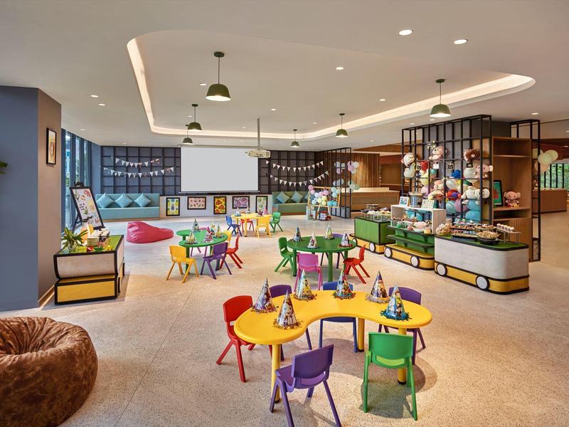 Área de juegos colorida y moderna para niños con mesas, sillas y decoraciones dulces en un hotel.