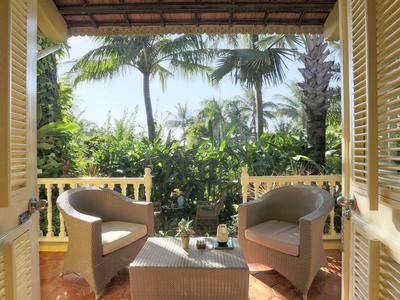 Balcony with two chairs, table, and view of tropical plants and palm trees.
