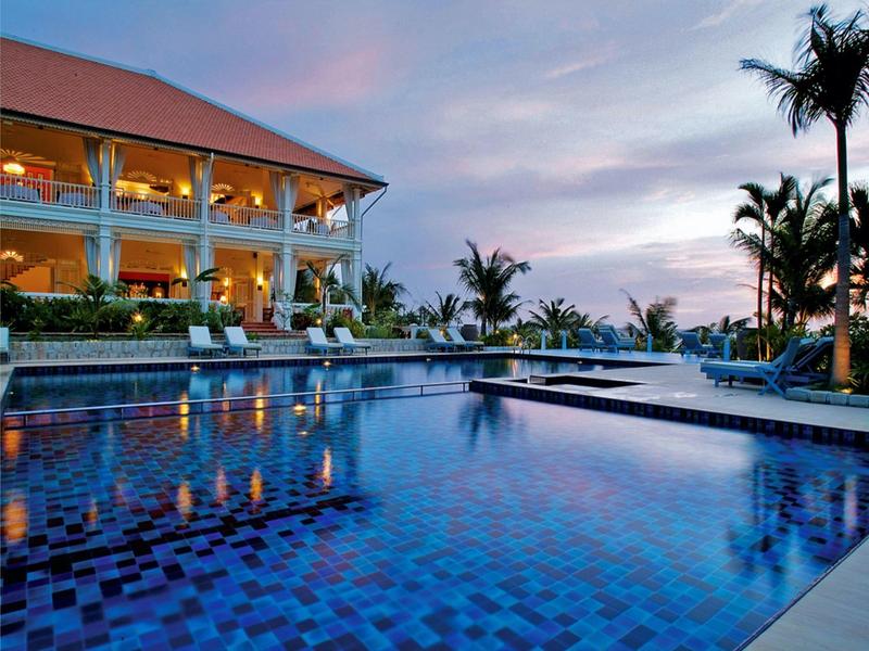 Luxurious pool with blue shimmering tiles beside a hotel building at sunset.