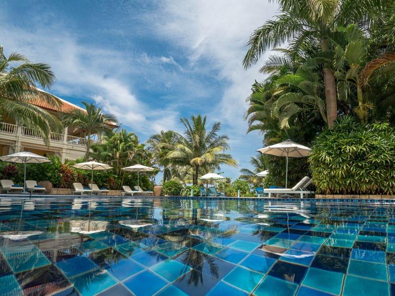 Luxurious pool area with blue tiles, palm trees, and lounge chairs under a bright sky