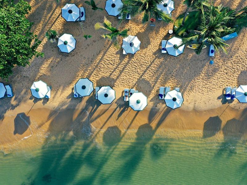 Aerial view of beach with umbrellas, shadows, and clear water.