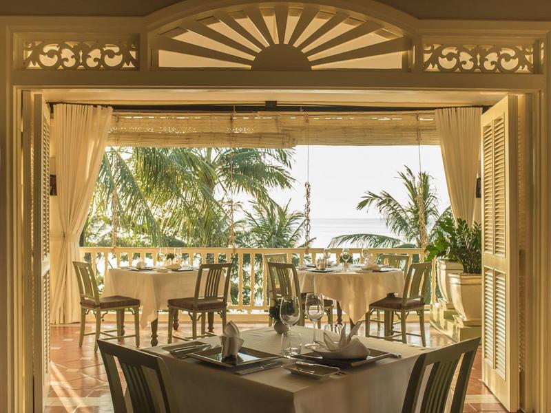 Restaurant with set table and view of palm trees and sea through open doors.