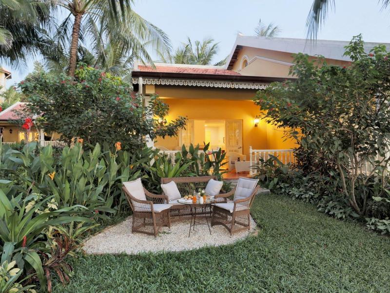Cozy outdoor seating area with four chairs on grass in front of a lit house and palm trees.