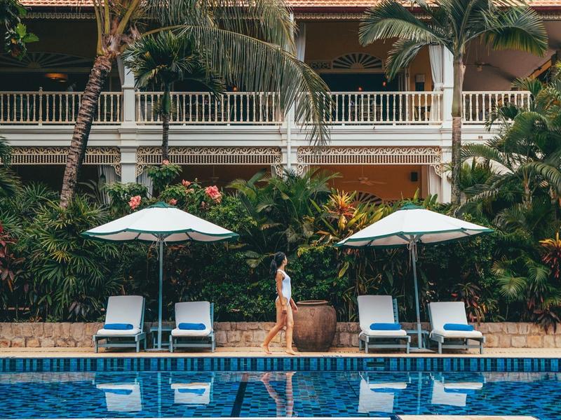 Hotel pool with lounge chairs, umbrellas, and exotic plant backdrop