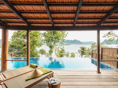 Relaxing infinity pool view from a wooden deck with lounge chairs under a tiled roof.
