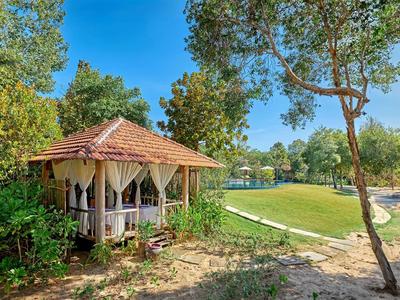 Wooden gazebo with curtains near beach and green lawn under blue sky.