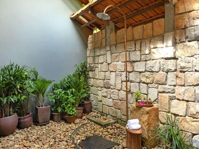 Cozy outdoor shower area with stone wall, wooden roof, and pebble ground with stepping stones.