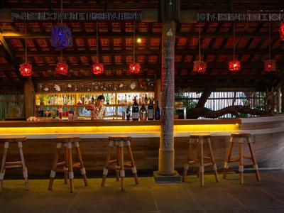 Cozy outdoor bar with wooden stools and warm lighting under a wooden roof.