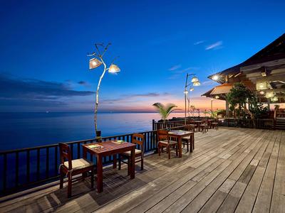 Wooden deck with tables and chairs by the sea at dusk with lampposts and a restaurant.