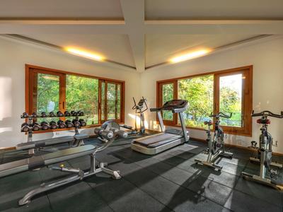 Modernes Fitnessstudio mit Trainingsgeräten vor großen Fenstern und Blick ins Grüne.