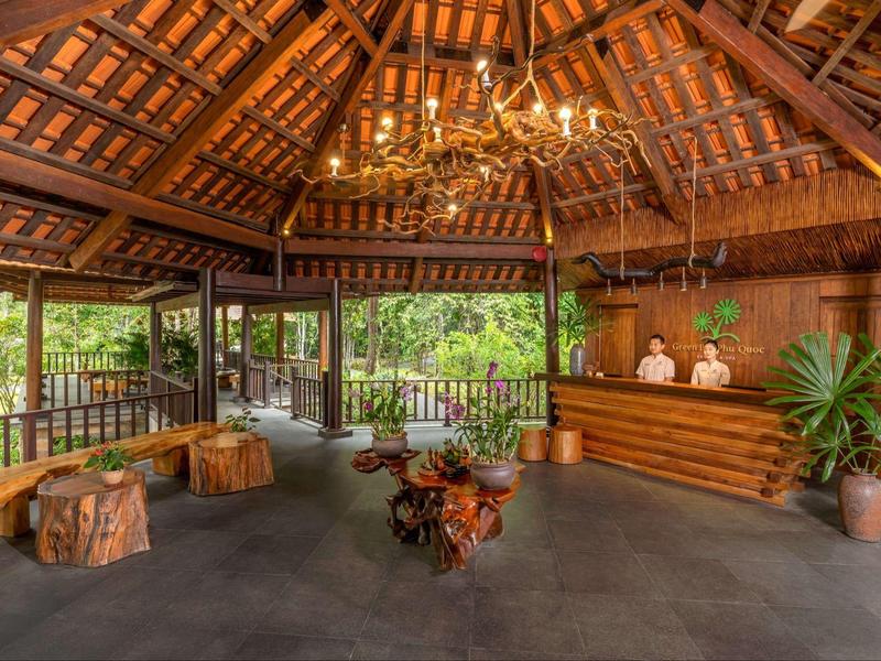 Rustic open-air hotel lobby with wooden beams, chandelier, reception desk, and natural wood furniture.
