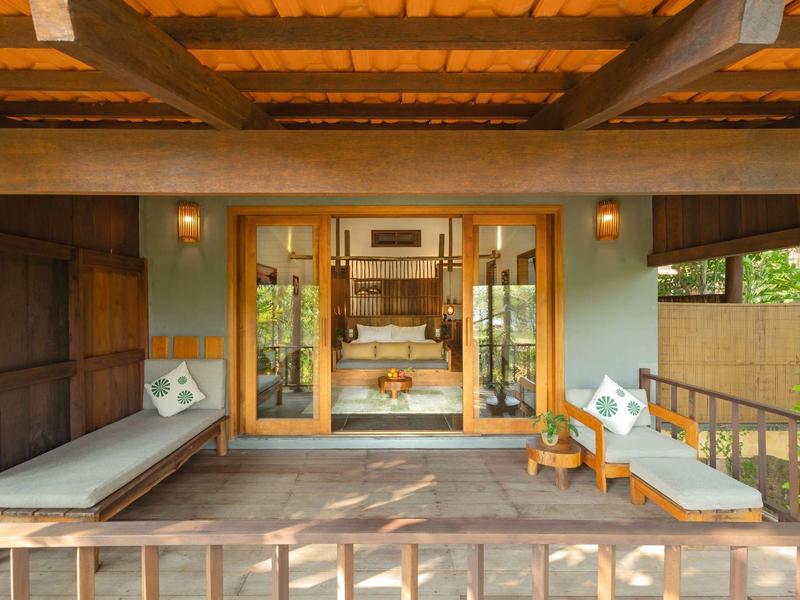 Cozy wooden terrace with lounge chairs and cushions overlooking greenery in a tropical setting.