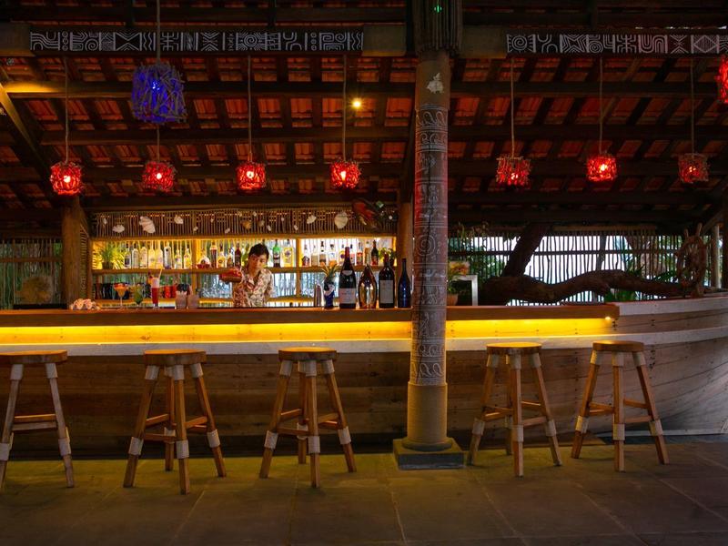 Cozy outdoor bar with wooden stools and warm lighting under a wooden roof.