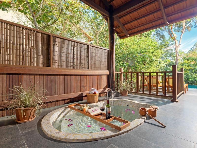 Outdoor wooden hot tub on a patio surrounded by greenery and bamboo privacy screen.