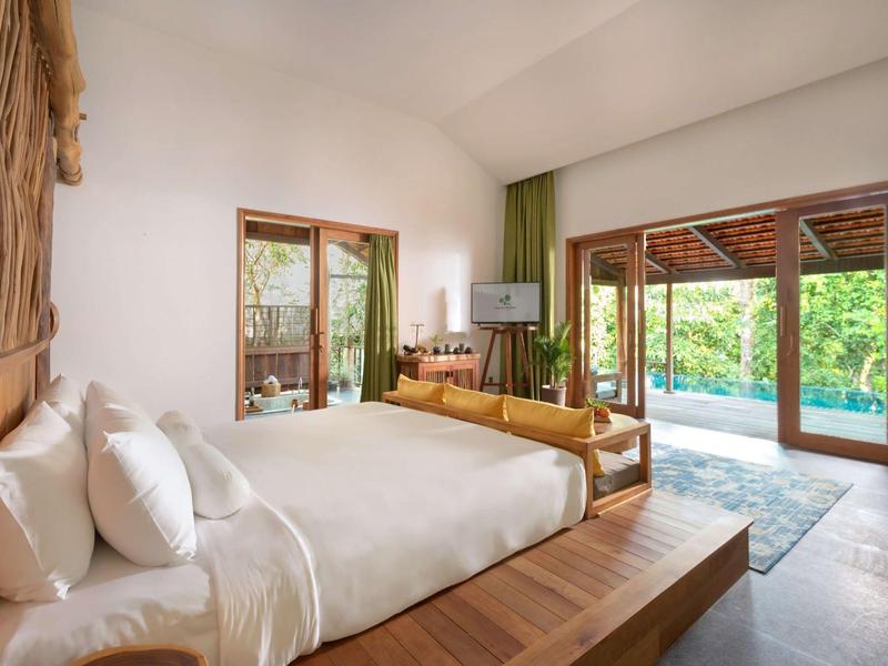 Spacious bedroom with wooden bed, seating area, and glass doors opening to a poolside patio.