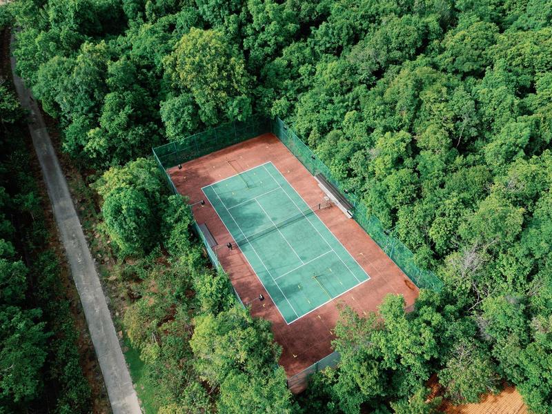 A secluded tennis court surrounded by dense green forest, seen from above.