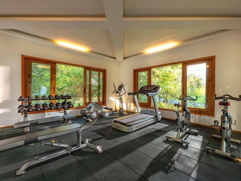 Bright gym with machines, weights, and large windows overlooking greenery.