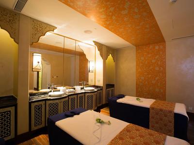 Sala de bienestar elegante con dos camillas de masaje y paredes doradas cálidas.