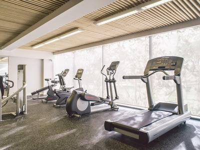 Helles Fitnessstudio mit Laufband, Crosstrainer und Fahrradergometer vor großen Fenstern.