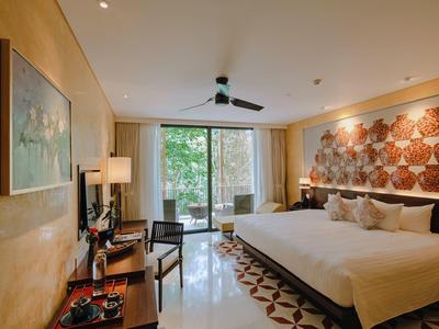 Habitación de hotel con cama grande, decoración en tonos cálidos y terraza con vista a jardín.