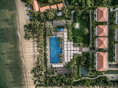 Vista aérea de un resort con piscina junto a una playa rodeada de árboles.