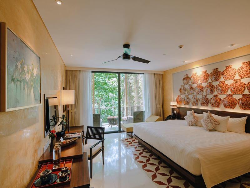 Habitación de hotel con cama grande, decoración en tonos cálidos y terraza con vista a jardín.