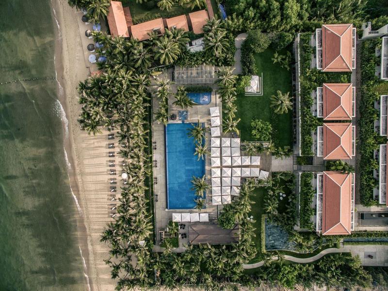 Vista aérea de un resort con piscina junto a una playa rodeada de árboles.