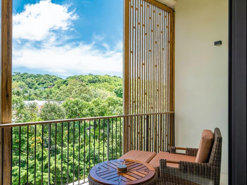Balcón con silla y mesa con vista a árboles verdes y cielo azul.