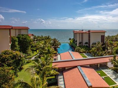 Blick auf ein Resort mit Pool, tropischer Vegetation und Meer im Hintergrund.