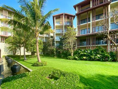 Grüner Garten mit Palmen und modernen Hotelgebäuden im Hintergrund unter blauem Himmel.