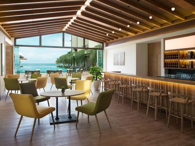 Moderner Restaurantbereich mit Holzdach, Gelbstühlen, Barhockern und Meerblick durch Glasfront.