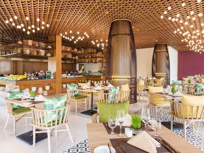 Modernes helles Restaurant mit Holzdecke, vielen Lampen und farbigen Stühlen an Tischen.