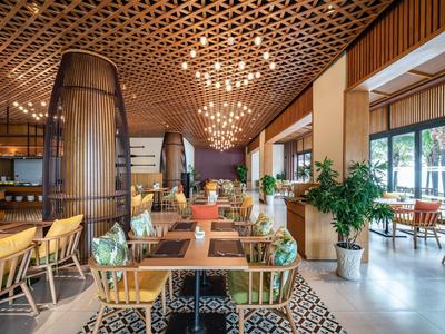 Modern eingerichteter Speisesaal mit Holzmöbeln, Pflanzen und Deckenbeleuchtung.