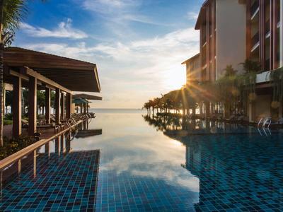 Luxuriöser Hotelpool mit Blick auf den Sonnenuntergang und Meer unter blauem Himmel.