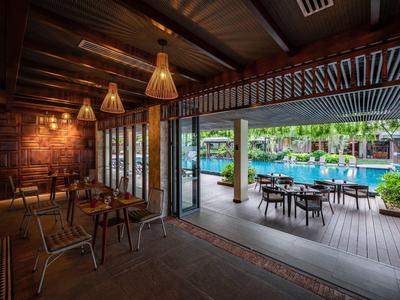 Gemütlicher Innenraum mit Holzmöbeln neben Terrasse mit Tischen und Pool im Hintergrund.