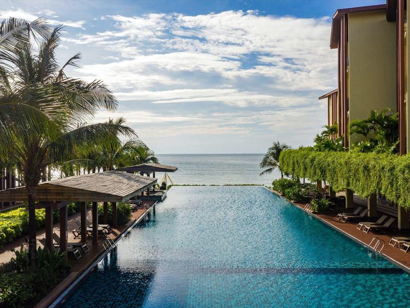 Infinity-Pool mit Meerblick und Palmen an einem sonnigen Tag in einem Hotelresort.